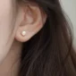 Femme avec Boucles d'Oreilles Perle Sertie à Griffes Acier 316L.