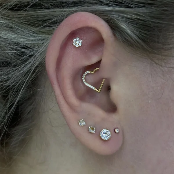 Femme portant un Piercing Cœur Asymétrique en Titane Anodisé Doré à Zircons Sertis au Daith Femme portant un Piercing Cœur Asymétrique en Titane Anodisé Doré à Zircons Sertis au Daith.