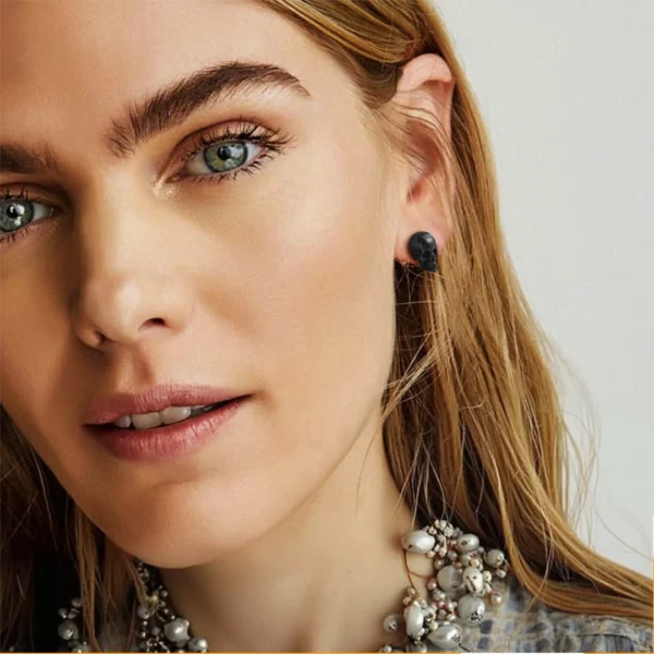 Femme portant des Boucles d’Oreilles Gothiques Têtes de Mort Acier Inoxydable Poli Effet Vieilli Finition Noire.