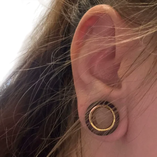 Femme avec un Écarteur Tunnel en Bois de Santal & Acier Doré au Lobe Femme avec un Écarteur Tunnel en Bois de Santal & Acier Doré au Lobe.